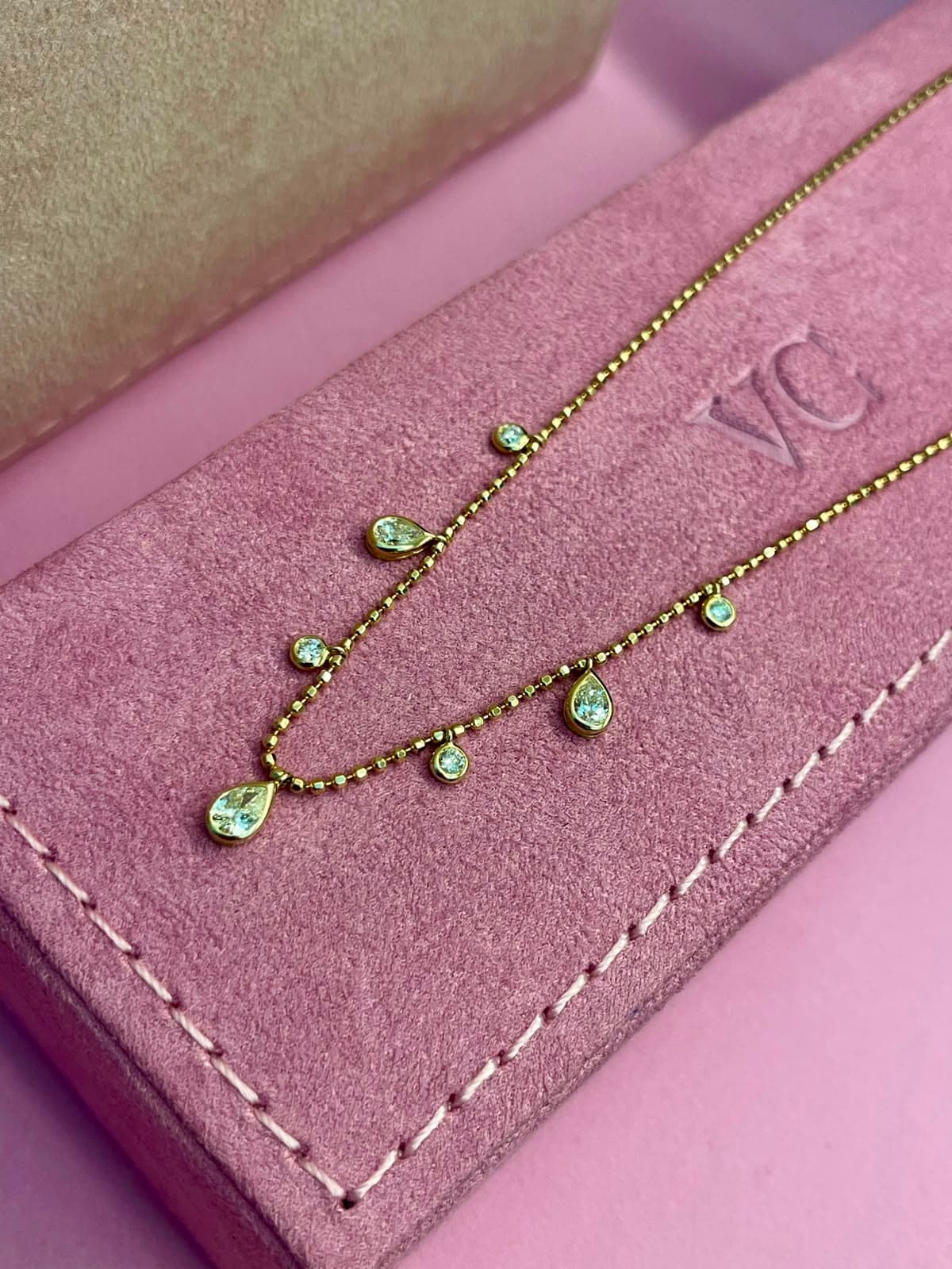 Colar de ouro com pingentes de diamantes em gota sobre estojo rosa com o monograma VC