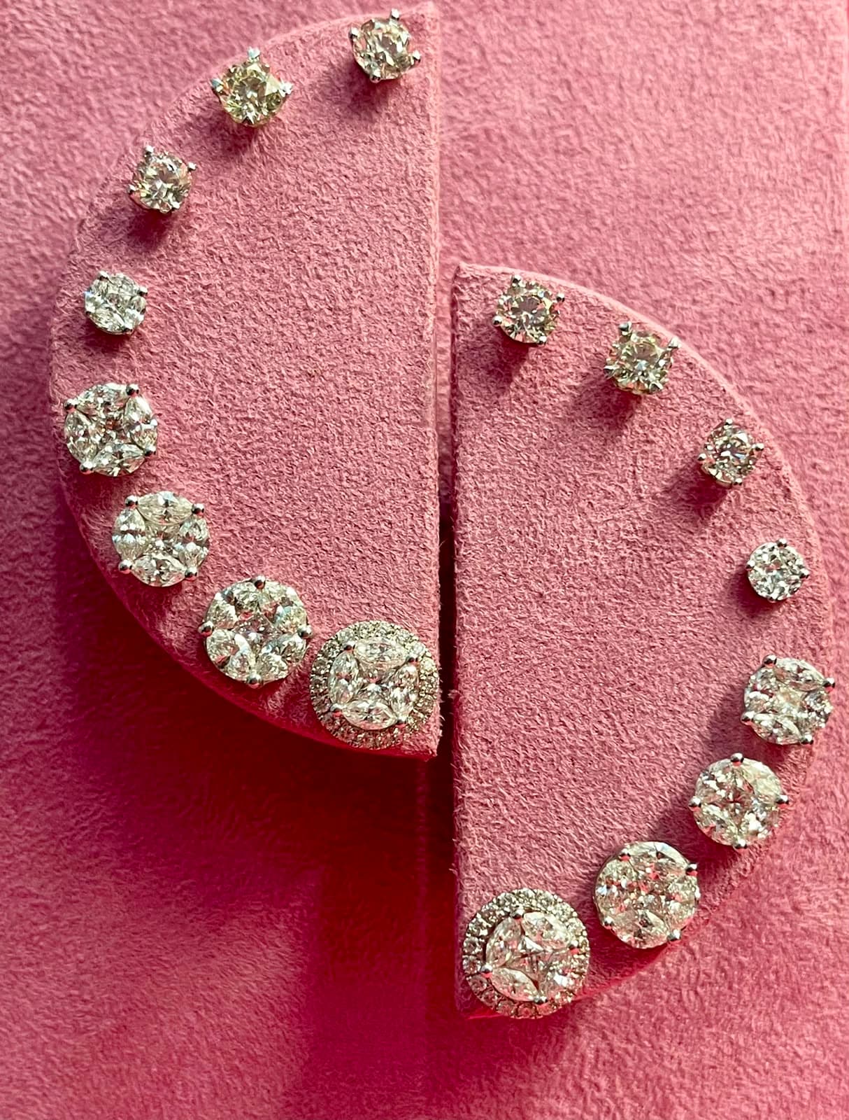 Brincos de diamantes em vários formatos alinhados sobre expositor de camurça rosa